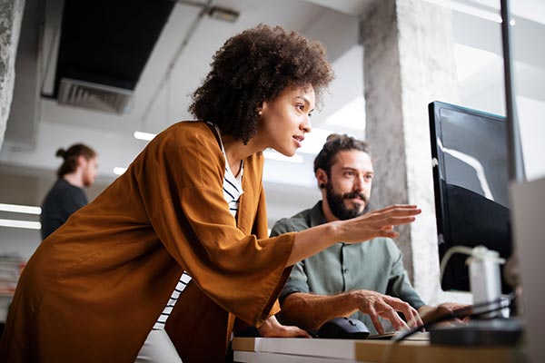 A contractor visiting a client on site at their office, looking at a client employee’s screen and advising them on the work they’re doing.
